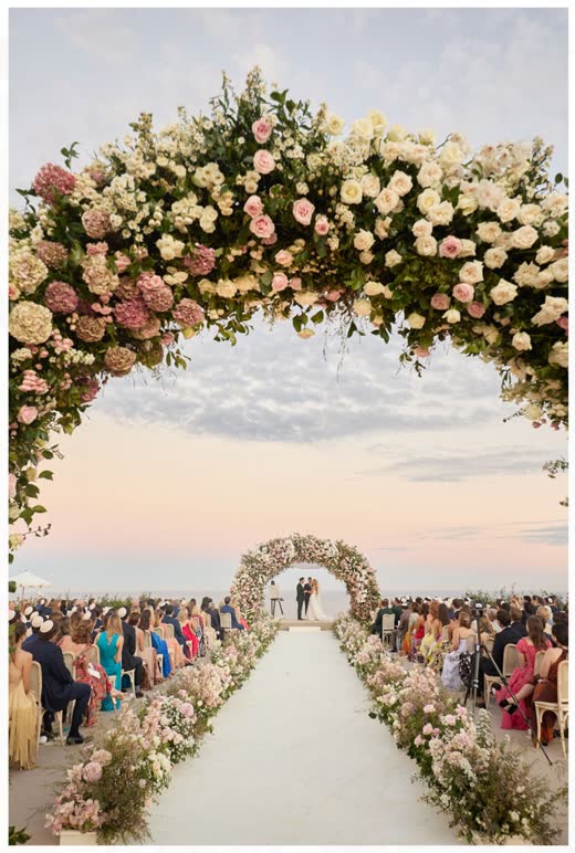 A flower arch framing a long aisle full of guests
