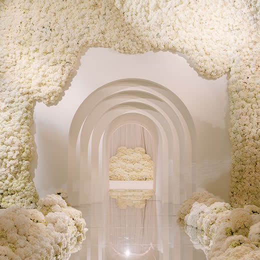 A tunnel of white flower-covered arches over a mirrored floor
