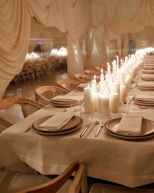A long table glowing with pillar candles under draped fabric