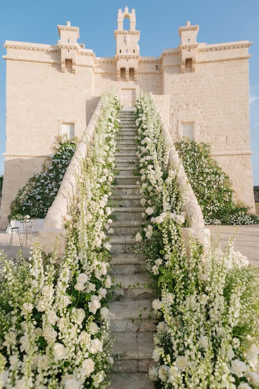 A stone staircase lined with white flowers up to a castle