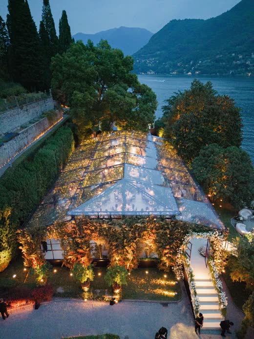 A glass tent lit up at night beside a lake