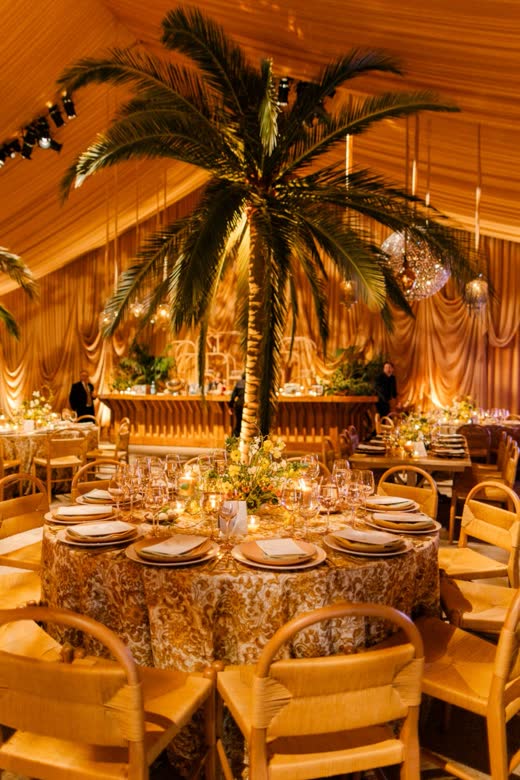 A tented dinner around a palm tree, lit gold